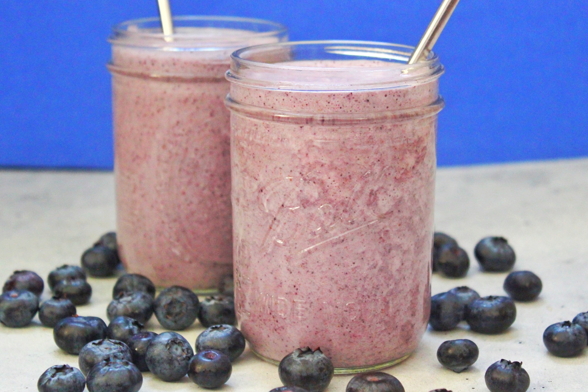 Two masons jars filled with blueberry-vanilla protein smoothie and straws in them. 