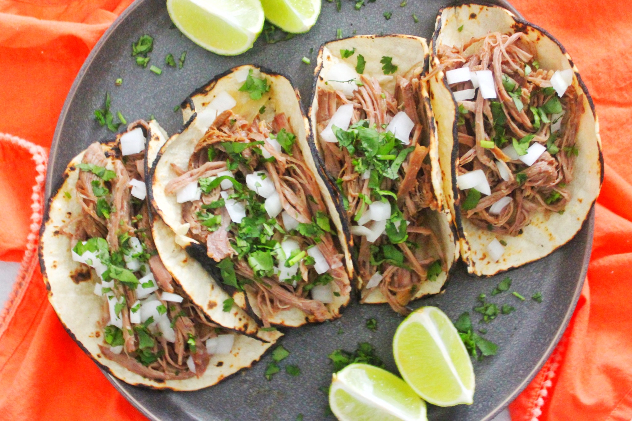 Slow Cooker Carne Asada Tacos topped with onions and fresh cilantro. Served on a gray plate. 