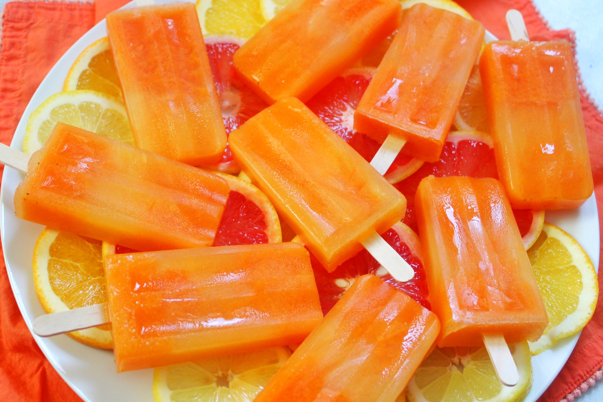 Throat Soothing Popsicles laying over sliced oranges, grapefruit and lemons. 