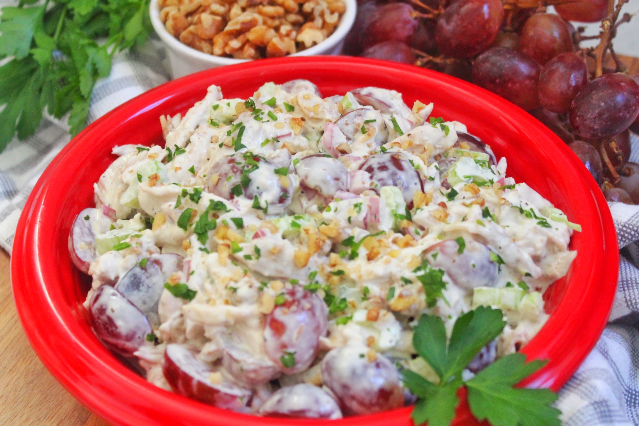 Chicken Salad with Grapes and Walnuts served in a red bowl. Walnuts and grapes in the background. 