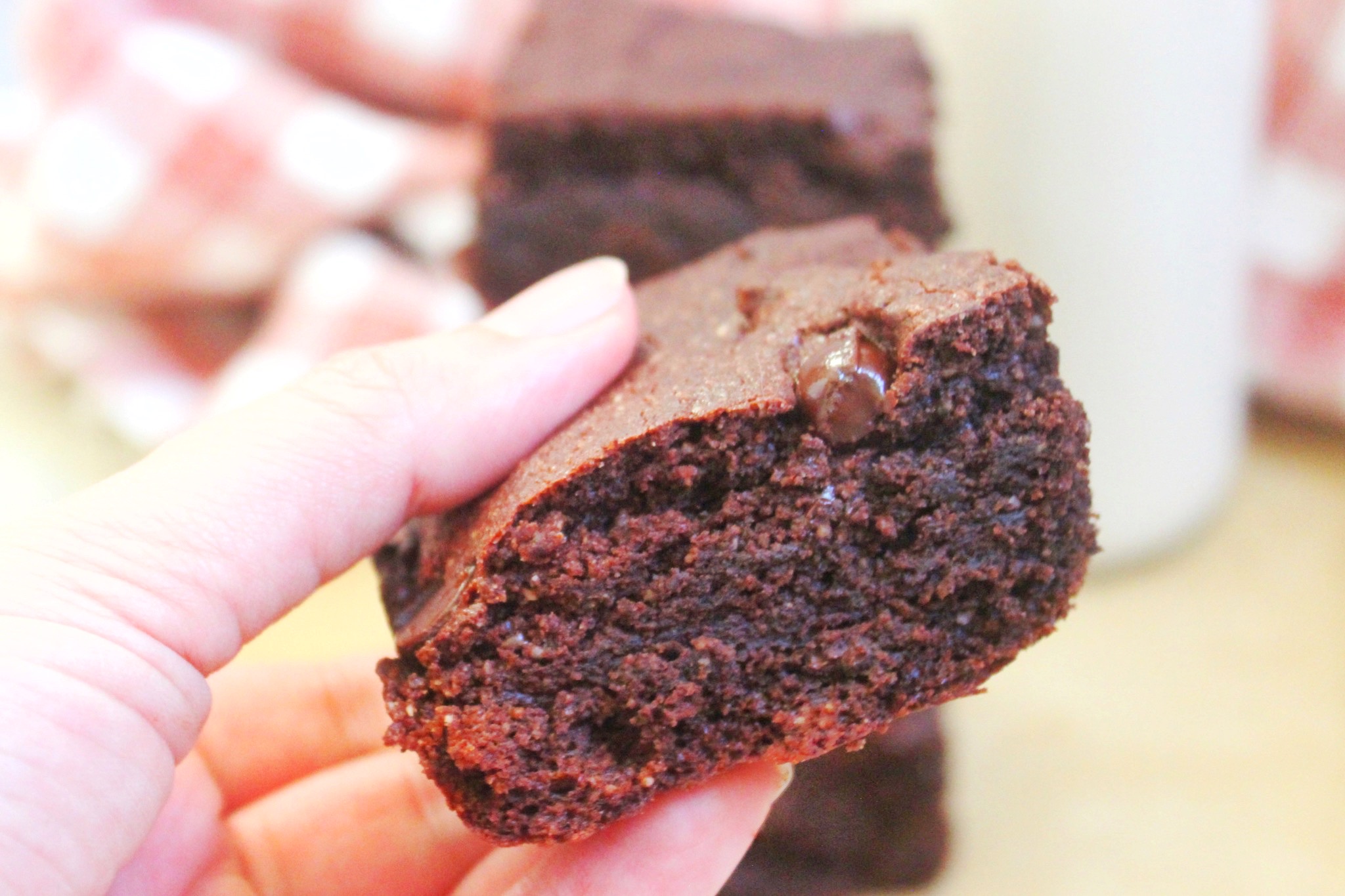 Hand holding a piece if gluten-free brownies. Stack of brownies in the background. 