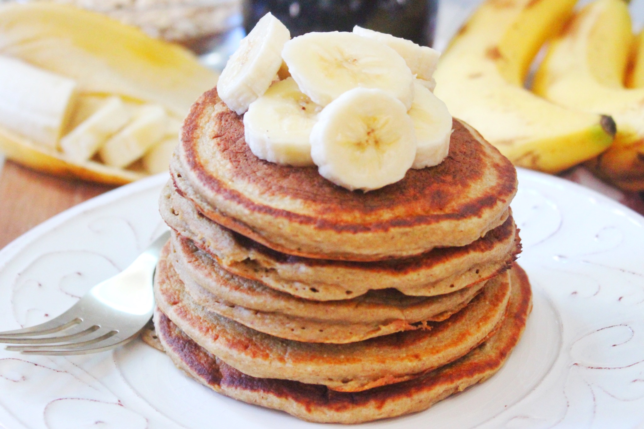 Stack of pancakes topped with banana slices on a white plate. 
