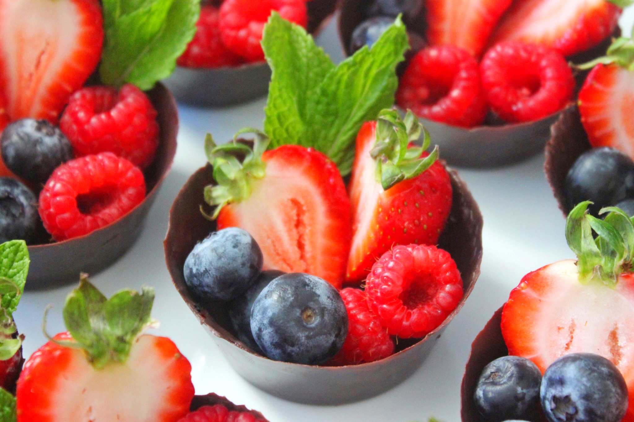 Chocolate cups filled with fresh berries placed over a white platter. 