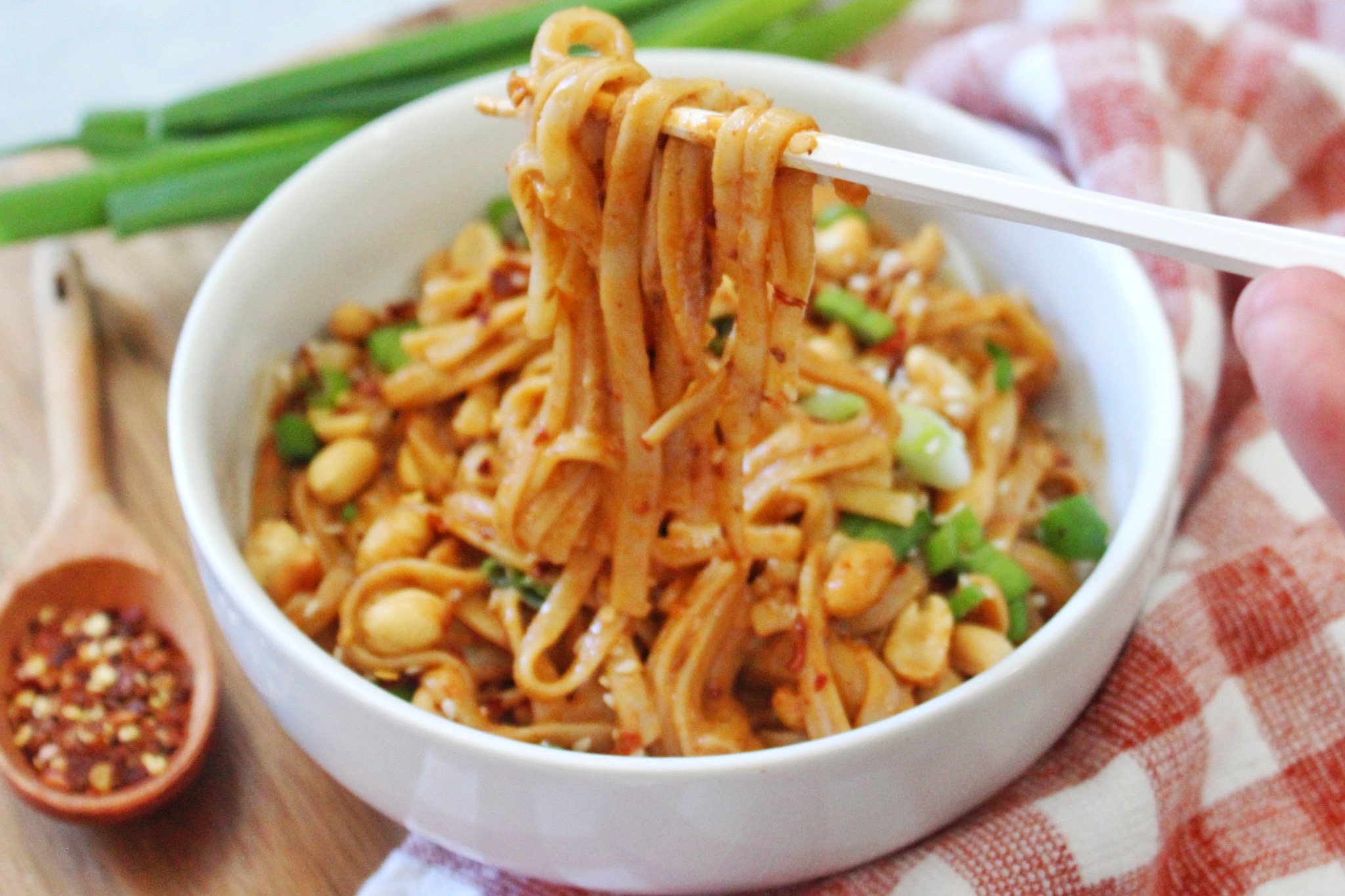 Spicy peanut noodles in a white bowl and twirled around with white chopped sticks. 